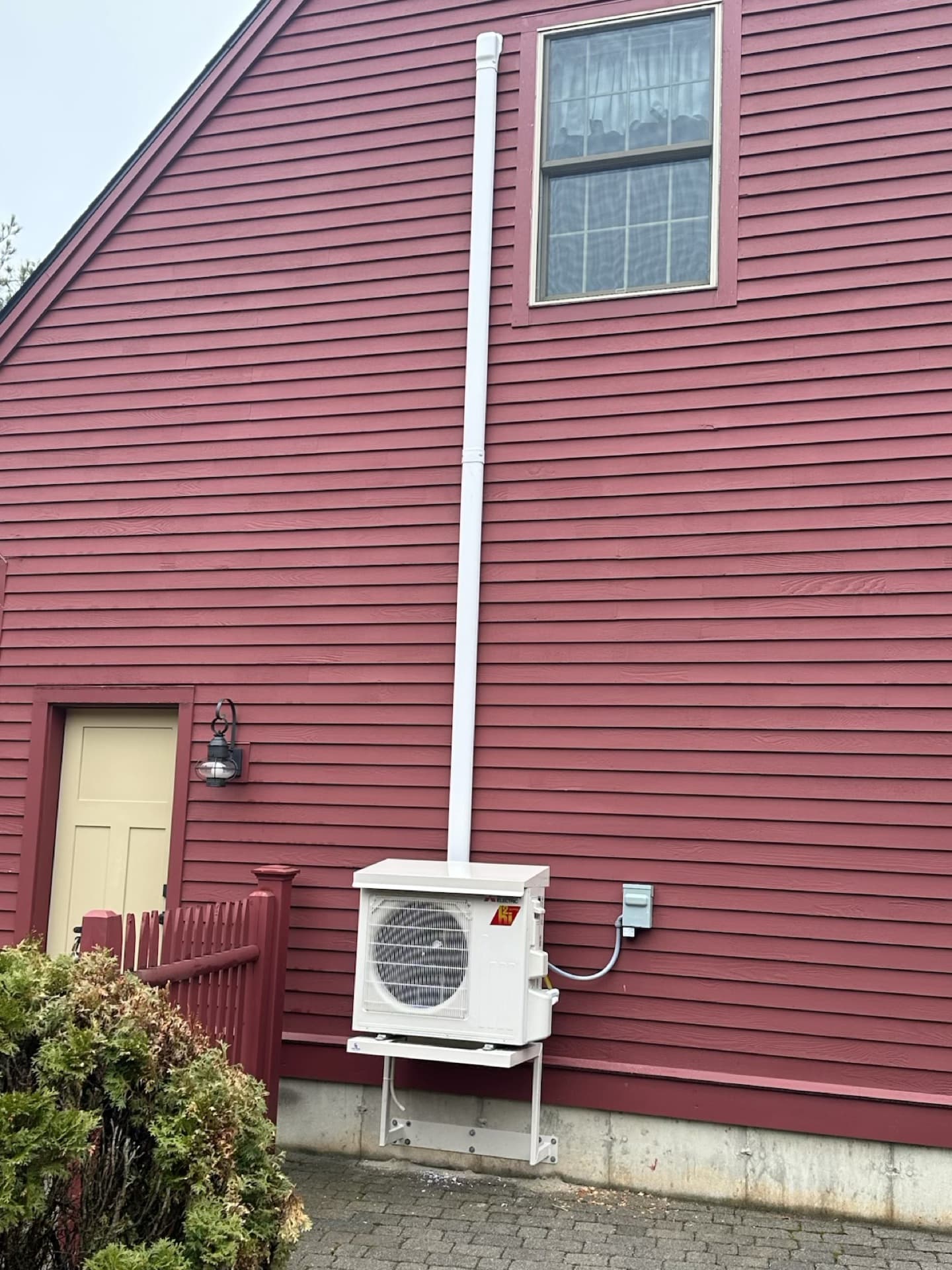 Wide view of outdoor heat pump unit and line set on a home exterior